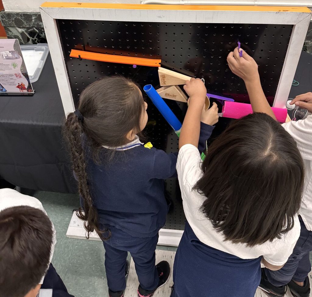 Young students working on a Rube Goldberg machine pegboard challenge.